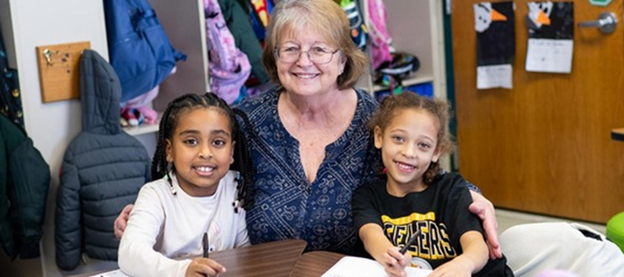 Adult seated with two elementary students