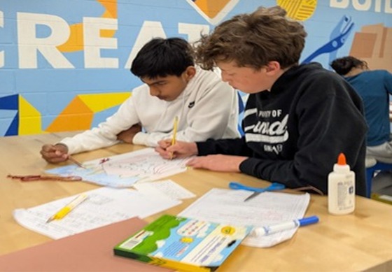 Students seated working together with pencils, markers, paper, and glue