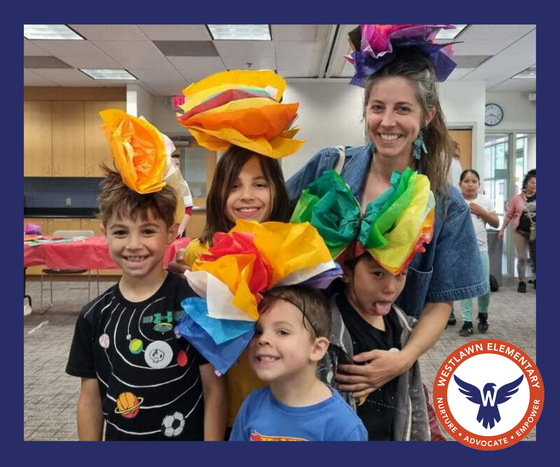 an adult stands with four students, all of them wearing brightly-colored hats made from tissue paper