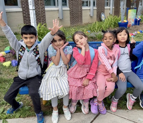 5 kindergarden students sitting on a bench in front of  the school