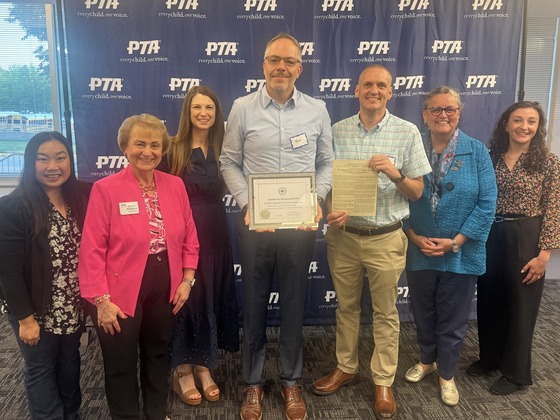 A group of seven school officials and PTA members posing together while holding a certificate at an awards ceremony.