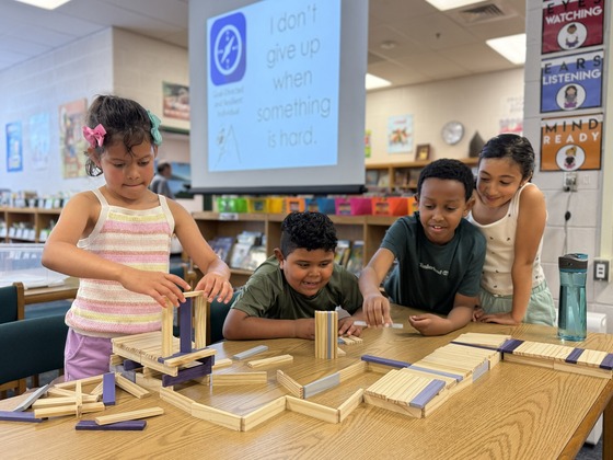Four elementary students working collaboratively to build a complex structure with wooden blocks in a school media center.