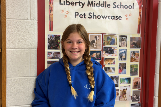 Student poses in front of the Liberty Middle School Pet Showcase display featuring student-submitted pet photos in the library.