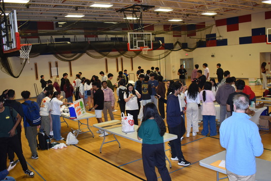 Wide angle photo of gym 2's J-Day activities. There are several tables set up as students visiting each one to purchase the items.