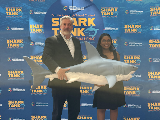 And adult man and high school girl hold a large fake shark. 