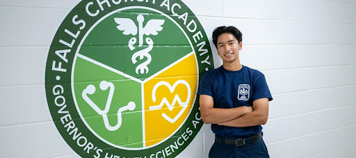 A male in EMT uniform stands next to a Falls Church Academy seal painted on a wall. 