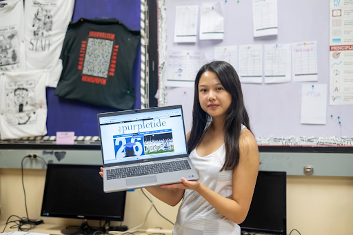 A girl holds up a laptop showing off the website of her school newspaper. 