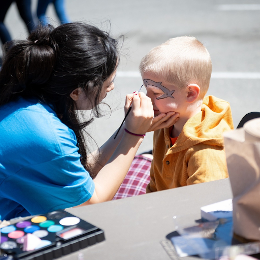Summer Extravaganza: A child sits while having a shark painted on his face by a young woman. 