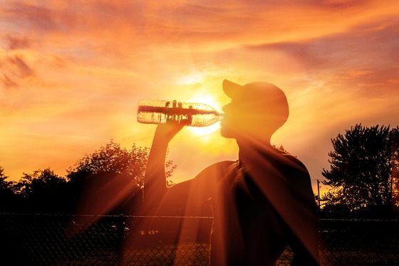 Photo of man drinking water with the sun beaming in the background
