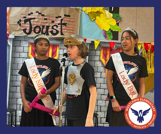 3 students stand on the JOUST! stage. 2 wearing sashes and crowns watch one wearing armor and a knight helmet. All 3 students hold boomwhackers.