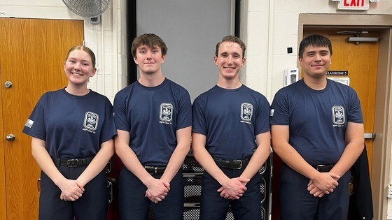 4 students standing together in Firefighting Academy T-shirts at graduation ceremony