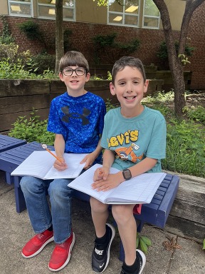 Two boys sitting in couryard with notebooks on their lap