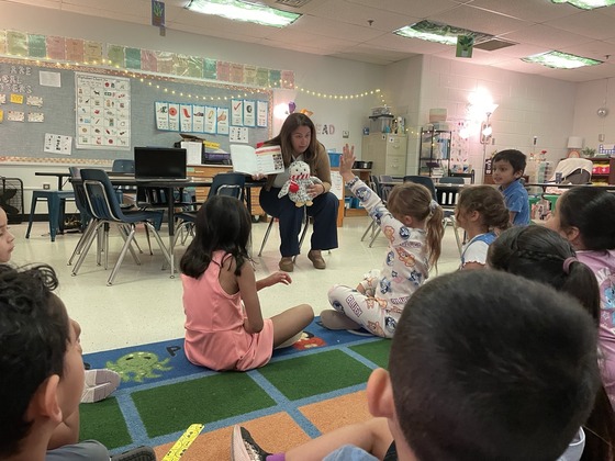 Principal Vereb Holding up book with a stuffed animal on her lap in front of kindergartners who are on the floor