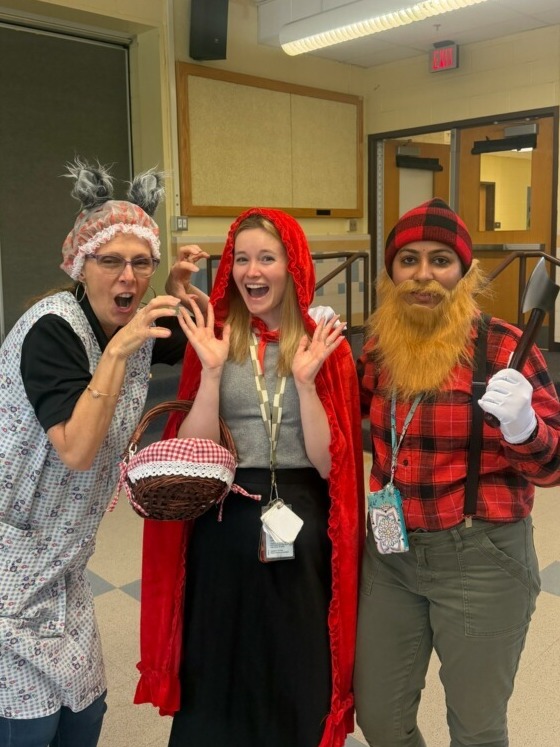Three of our 2nd-grade staff members smiling in Little Red Riding Hood costumes: the Wolf, Red Riding Hood, and the Woodsman.