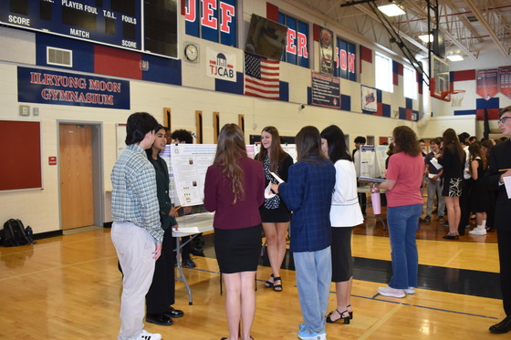 Group of freshmen explaining their poster board project in gymnasium