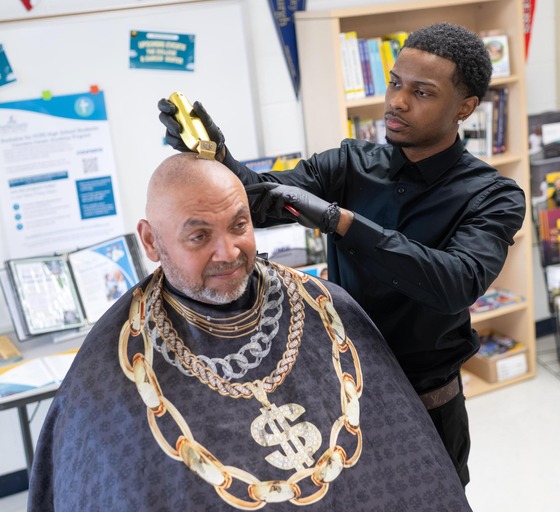 Male student cutting adult male's hair