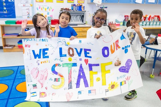 students with a sign that reads "we love our staff!"