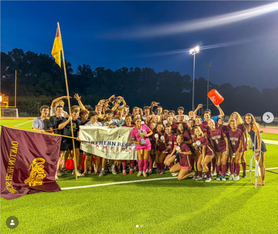 Girls Soccer team kneeling and standing together while holding trophy and Northern Region Champions banner