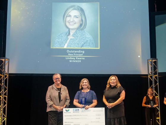 Three women standing together smiling while one holds oversized check