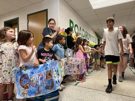 Younger students cheer and hold a congratulatory banner as sixth graders participate in a school promotion walk.