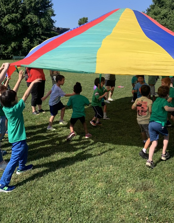 Students racing under a rainbow parachute while enjoying field day.