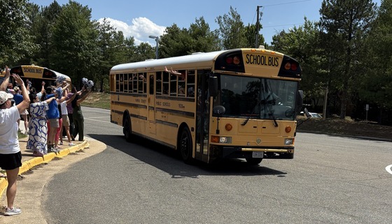 Staff members waving at students on the bus as it pulls out of the bus loop