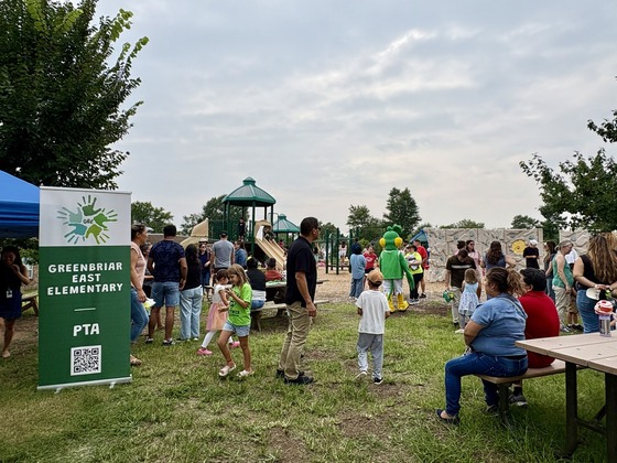 Kindergarten families gather near the playground with the Greenbriar East mascot during Popsicles on the Playground.