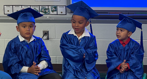 Three students in preschool wearing a blue cap and gown for their graduation from PAC