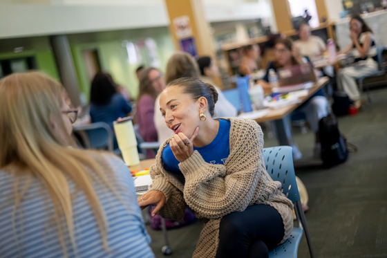 A teacher talks with a colleague at a table in a library.