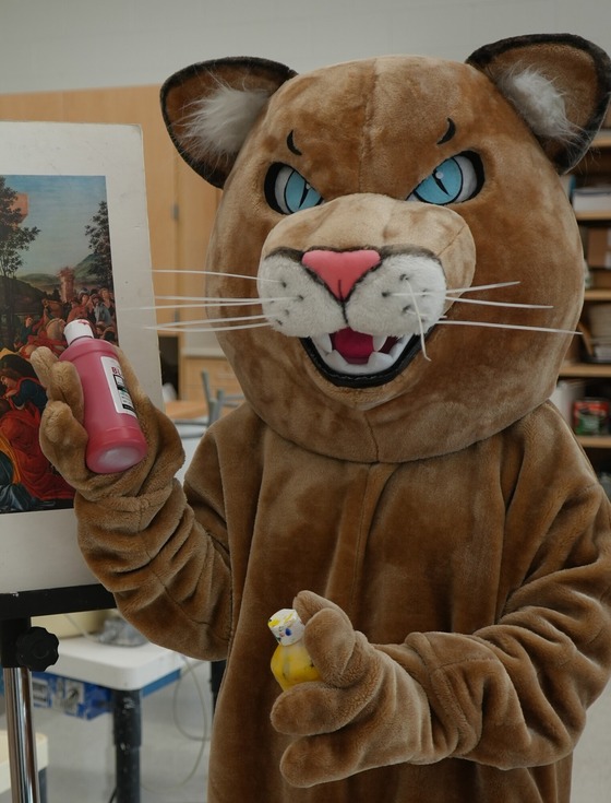 cougar mascot with paint bottles in front of a canvas