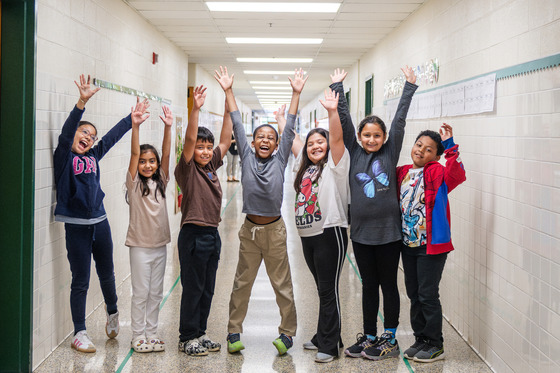 Happy kids raise their hands in a hallway.