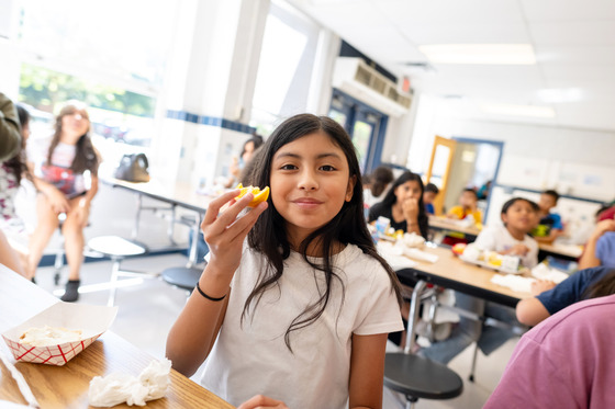 A girl smiles while eating an orange.