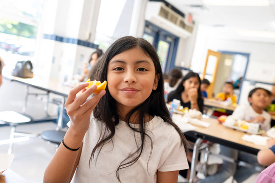 A girl smiles while eating an orange.