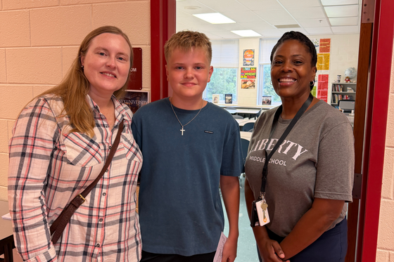 A school staff member in a grey Liberty Middle School t-shirt standing in a doorway alongside a student and an adult family member.
