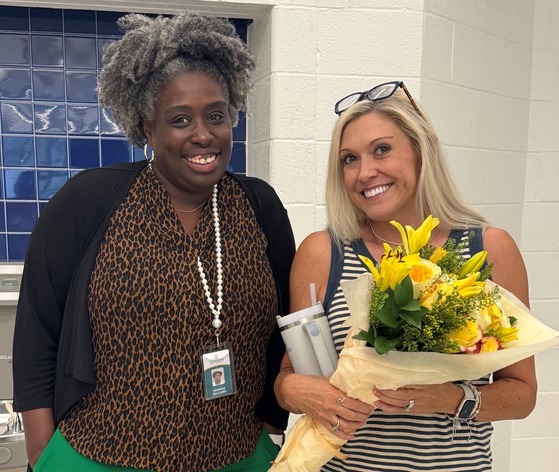 Two employees standing, one with a bouquet of flowers
