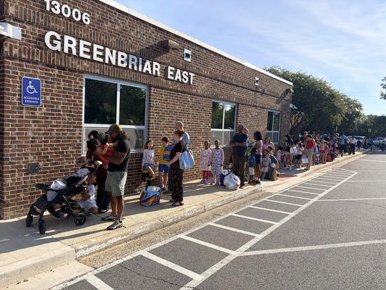 Students and families carrying school supplies line up outside Greenbriar East for Open House.