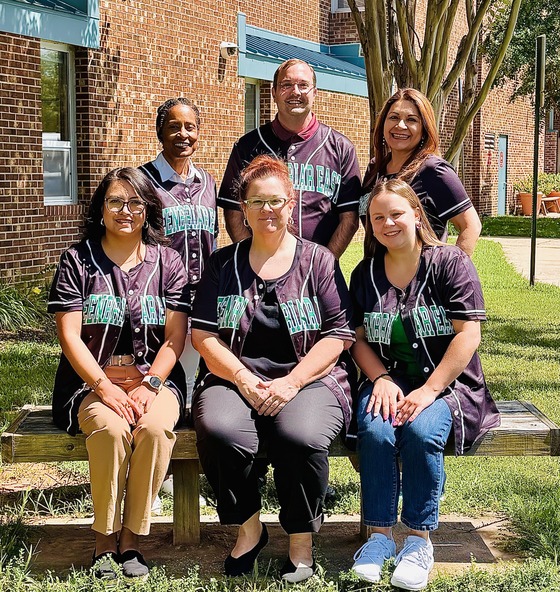 Greenbriar East’s office staff poses together outdoors in matching school baseball jerseys.