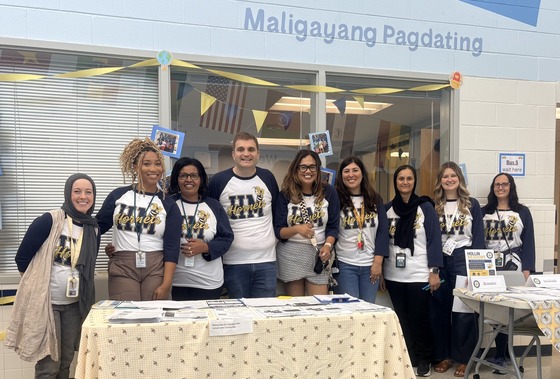 A group photo of the HMES admin team and some of the staff standing behind the information tables.