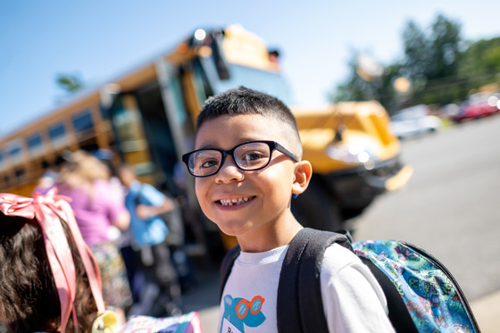 A young boy wearing a backpack smiles. 