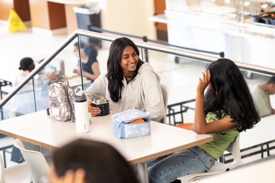 Two girls smile while eating lunch at school. 