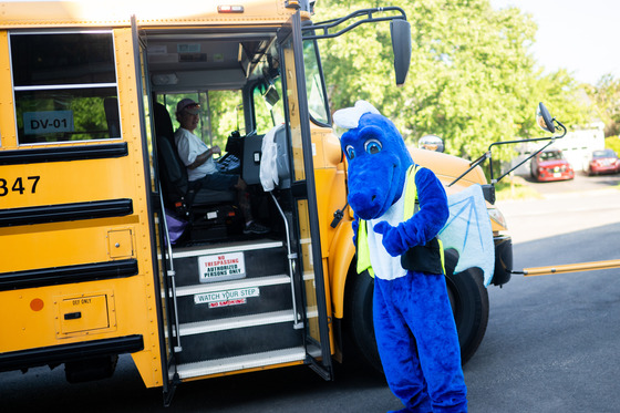 A dragon mascot stands outside a school bus