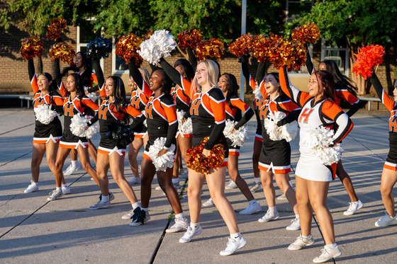 Cheerleaders cheer outside a school. 