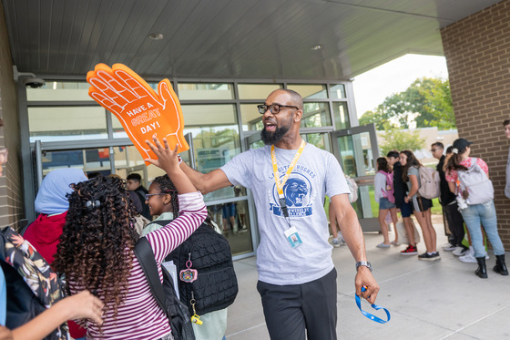 A principal wearing a giant foam hand high fives middle school students.