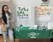 One student stands to the left of two trifold presentation boards about plastic waste