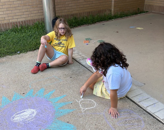 Students drawing pictures with chalk on the sidewalk near the bus loop to welcome students back
