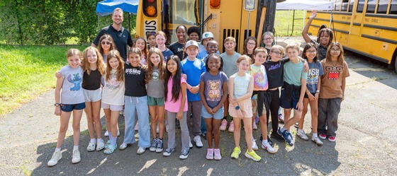 SLES Students posing for a picture in front of a turned over school bus as they train to become patrols.