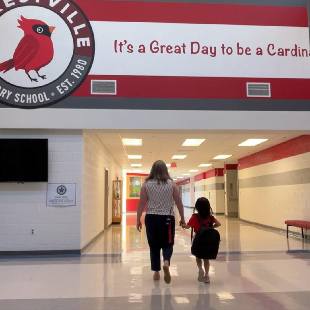 A teacher and student walking in the hallway under a mural that states "It's a Great Day to be a Cardinal"