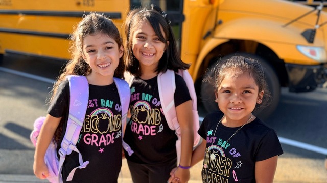 3 young students smiling holding hands on the first day of school