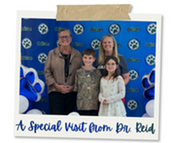 Dr. Reid and Principal Kelley stand with two smiling children in front of an Oakton Elementary backdrop