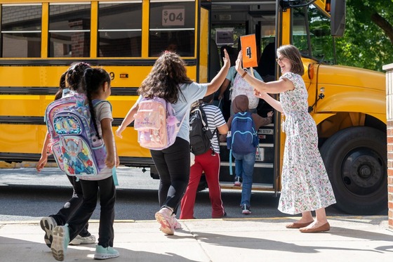 librarian high fives students as they get on the school bus after a school day